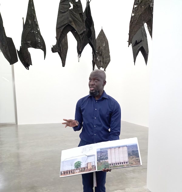 Ibrahim Mahama explains his process using his notebooks with images of silos, in front of ‘Lazarus’, 2021