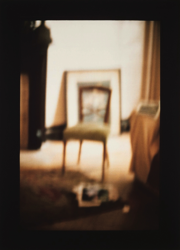 David Armstrong, Jefferson Avenue, Brooklyn, 1997, Cibachrome © David Armstrong. Courtesy of the Estate of David Armstrong [An out-of-focus photograph of a wooden chair in a golden-lit room decorated with curtains, a carpet, and a framed artwork leaning against the back wall.]